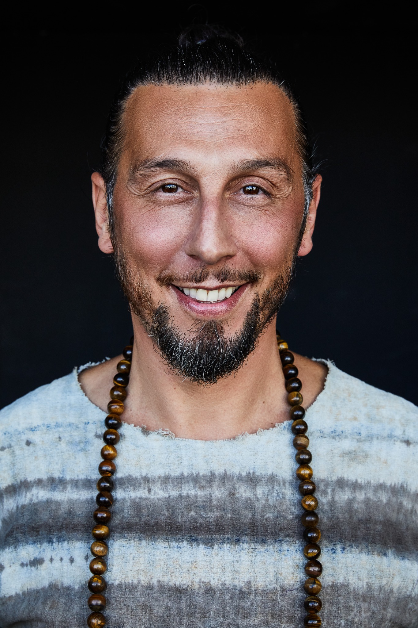 Ali mit zurückgebundenen Haaren, gemustertem Oberteil und einer Perlenkette.