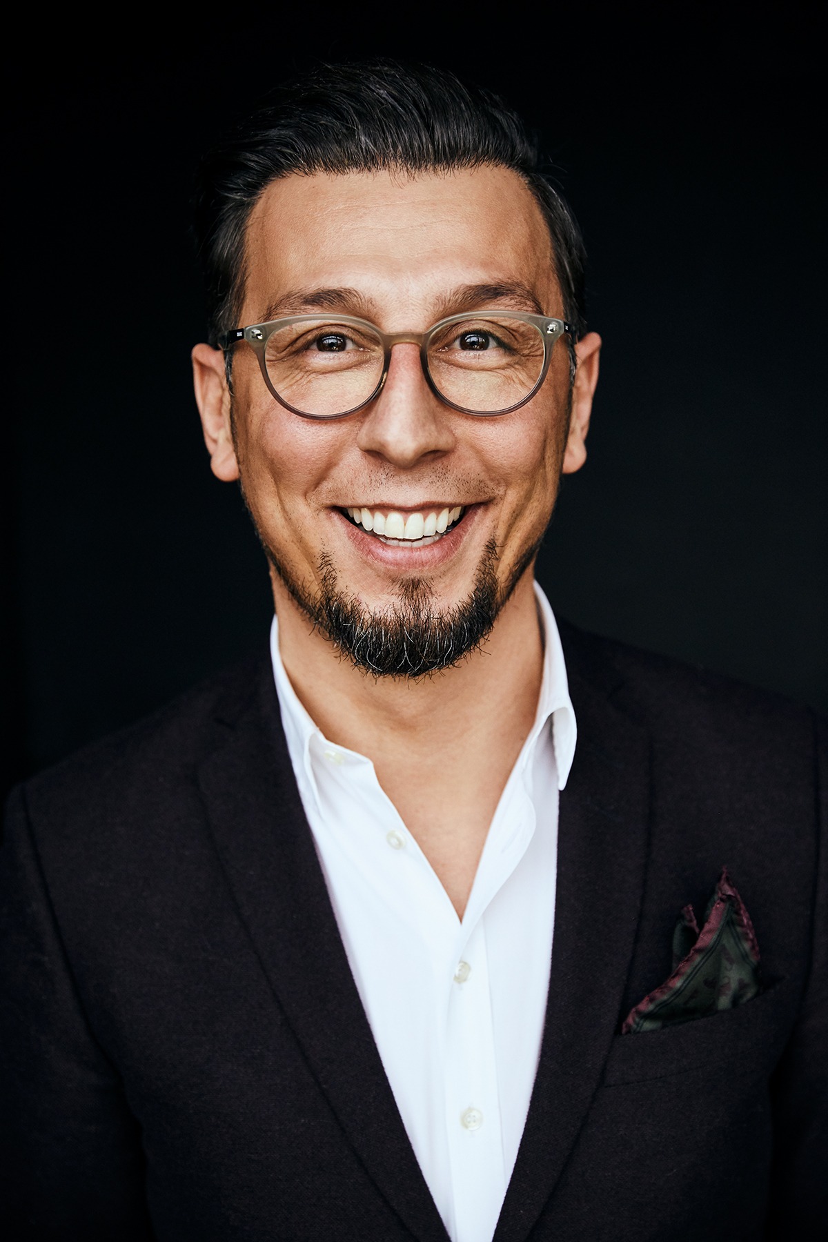 Ali in einer früheren Lebensphase, mit Brille, weißem Hemd und dunklem Sakko.