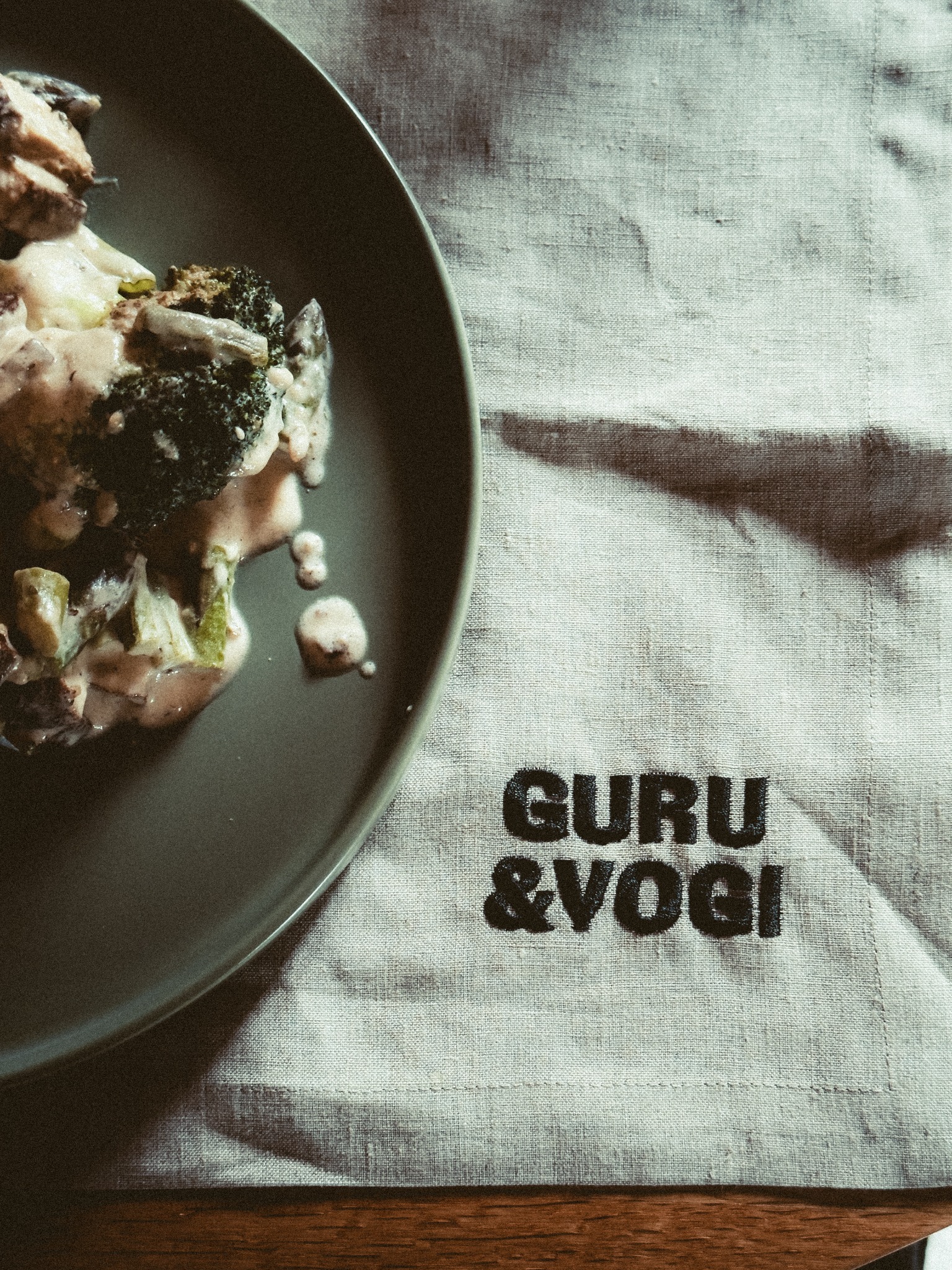 Ein Teller mit Gemüse neben einer Leinenserviette mit GURU & YOGI-Stickerei.