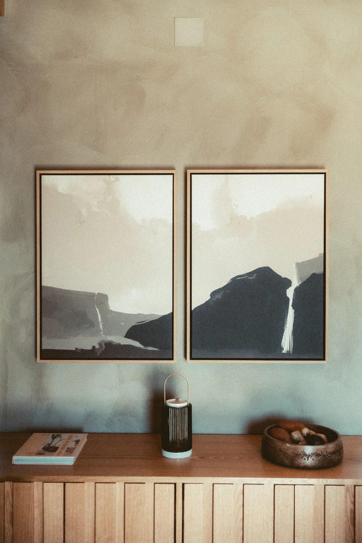 Landschaftsbilder und eine Eichenkommode vor einer natürlichen Wand.