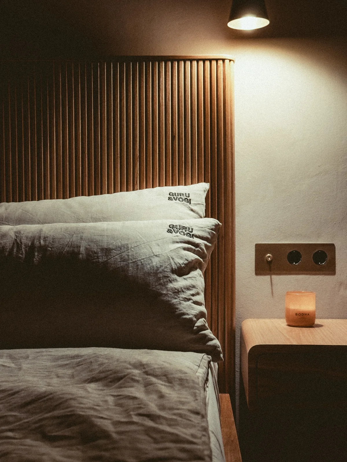 Leinenbettwäsche, Holzkopfteil und warmes Licht im Schlafzimmer.